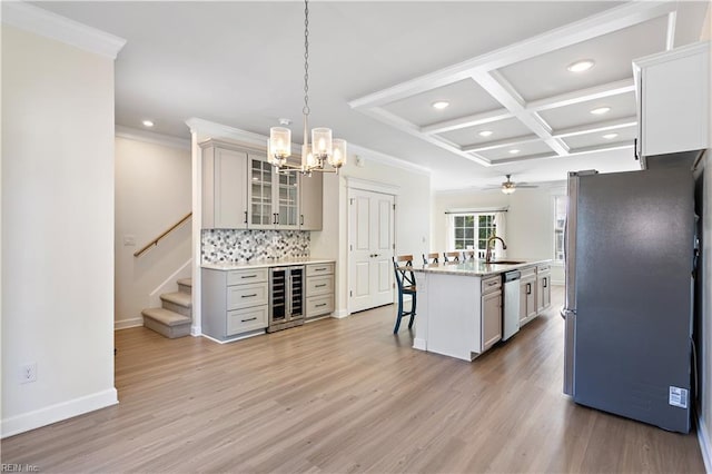 kitchen with appliances with stainless steel finishes, a breakfast bar area, wine cooler, hanging light fixtures, and a kitchen island with sink