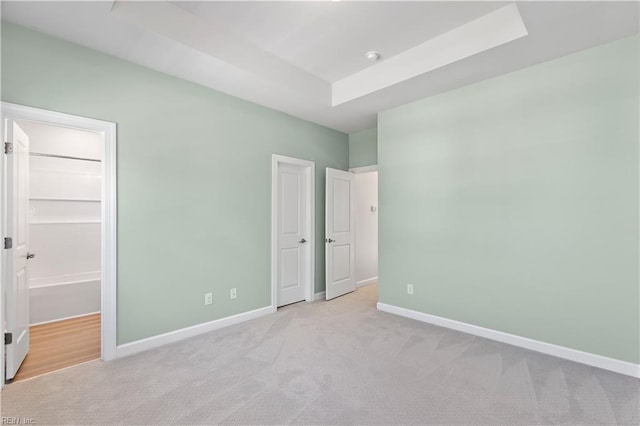 unfurnished bedroom featuring light colored carpet and a raised ceiling