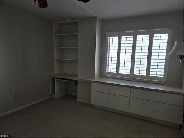 unfurnished office with built in desk, ceiling fan, and carpet