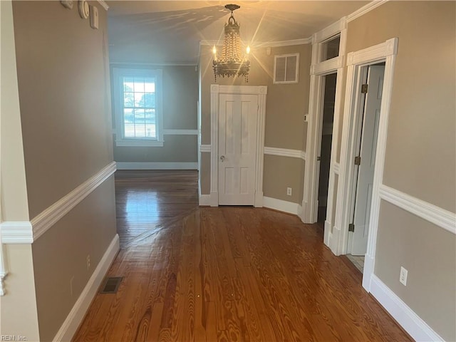 interior space with dark wood-type flooring, crown molding, and a notable chandelier