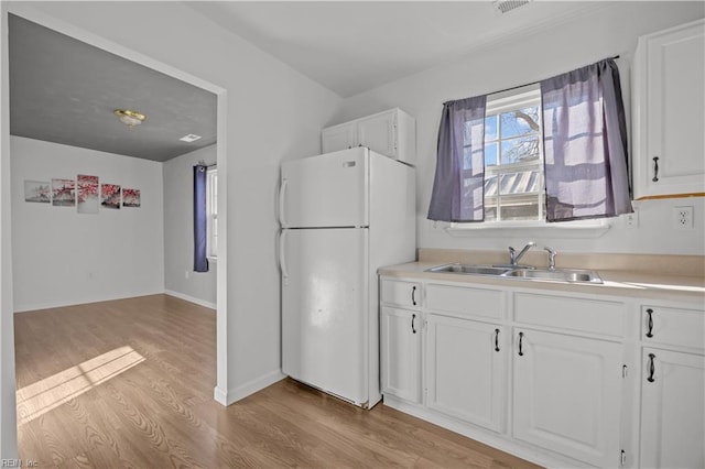 kitchen with white refrigerator, white cabinetry, sink, and light wood-type flooring