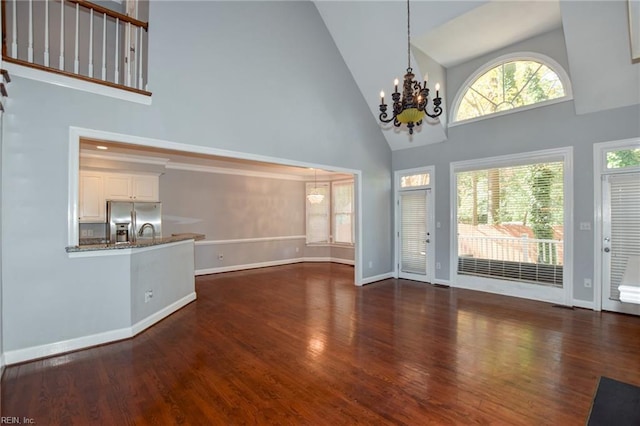 unfurnished living room featuring dark hardwood / wood-style flooring, high vaulted ceiling, and an inviting chandelier