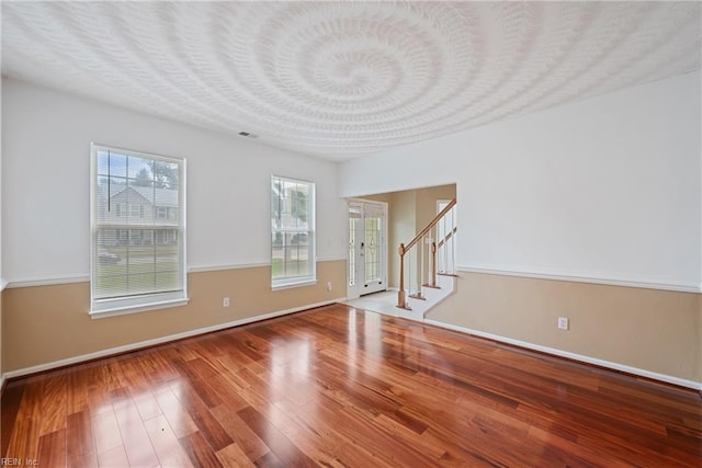 unfurnished room featuring a textured ceiling, stairs, baseboards, and wood finished floors