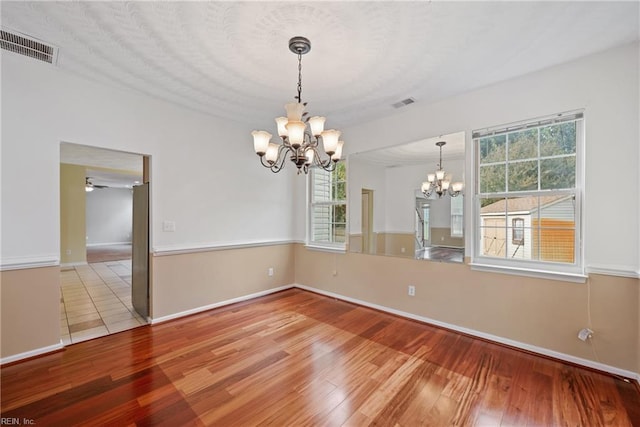 spare room with light wood finished floors, baseboards, visible vents, and ceiling fan with notable chandelier