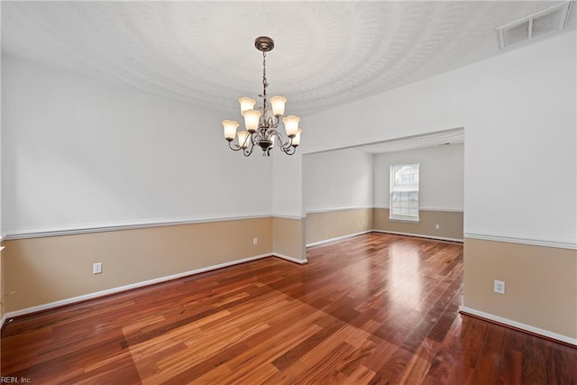 unfurnished room with an inviting chandelier, baseboards, visible vents, and wood finished floors