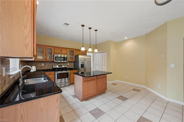 kitchen featuring a sink, appliances with stainless steel finishes, a center island, glass insert cabinets, and pendant lighting