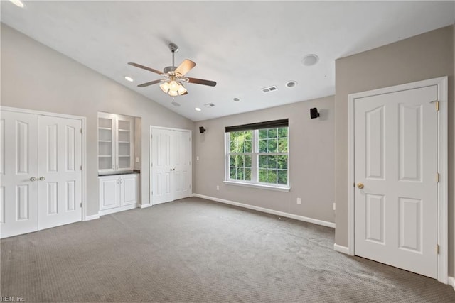 unfurnished bedroom featuring carpet floors, visible vents, vaulted ceiling, and multiple closets