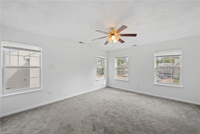 carpeted spare room with a ceiling fan, a wealth of natural light, visible vents, and baseboards