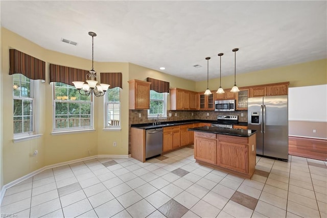 kitchen featuring appliances with stainless steel finishes, a center island, dark countertops, glass insert cabinets, and pendant lighting