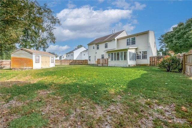 back of property featuring a storage shed, a lawn, a sunroom, a fenced backyard, and an outbuilding