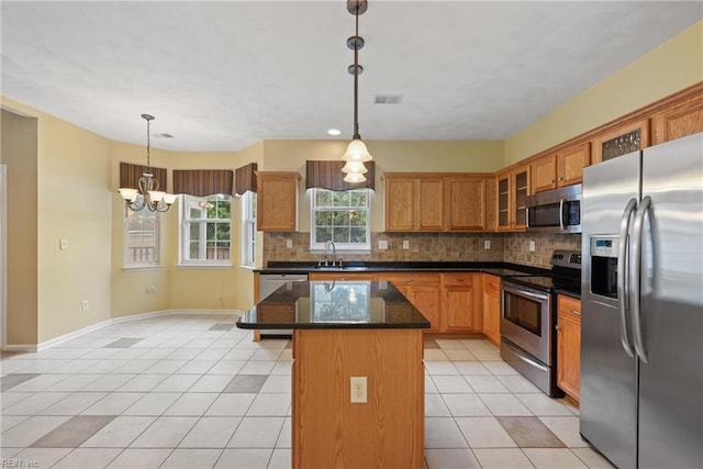 kitchen featuring hanging light fixtures, appliances with stainless steel finishes, glass insert cabinets, a kitchen island, and a sink