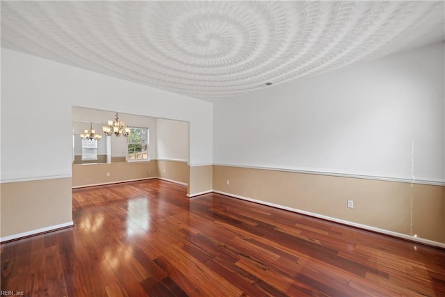 empty room with a textured ceiling, baseboards, wood finished floors, and an inviting chandelier