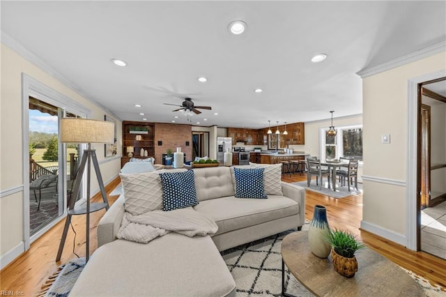 living room featuring crown molding, ceiling fan with notable chandelier, and light wood-type flooring