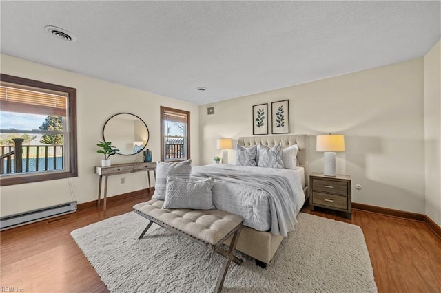 bedroom with multiple windows, a baseboard radiator, and light wood-type flooring