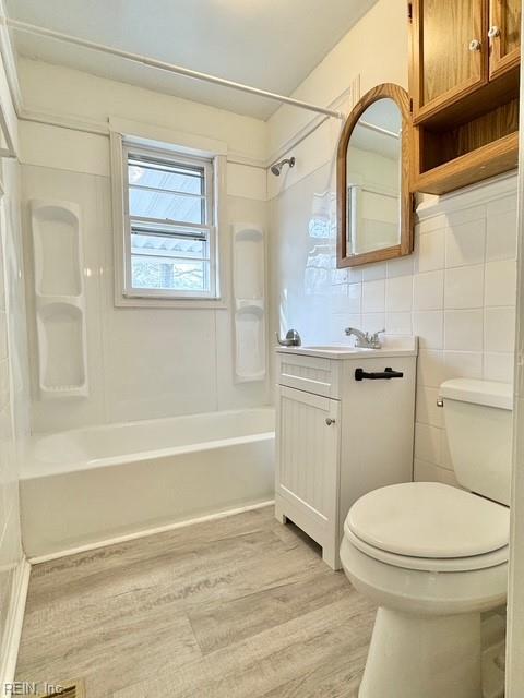 full bathroom featuring toilet, wood-type flooring, tile walls, shower / bathtub combination, and vanity