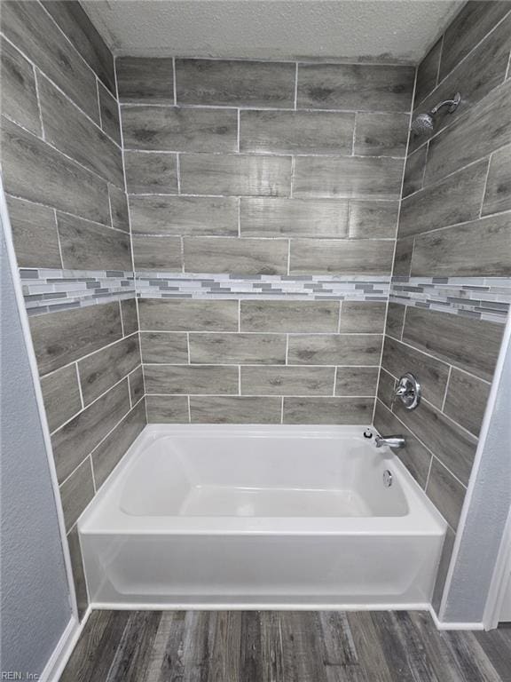 bathroom with hardwood / wood-style flooring, tiled shower / bath, and a textured ceiling