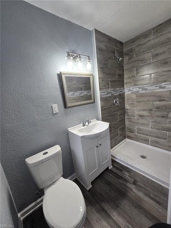 bathroom with toilet, a textured ceiling, a tile shower, vanity, and hardwood / wood-style flooring