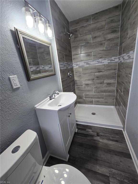 bathroom with vanity, wood-type flooring, toilet, and tiled shower