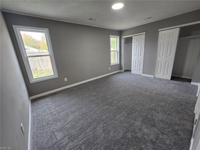 unfurnished bedroom with ornamental molding, dark carpet, a textured ceiling, and two closets