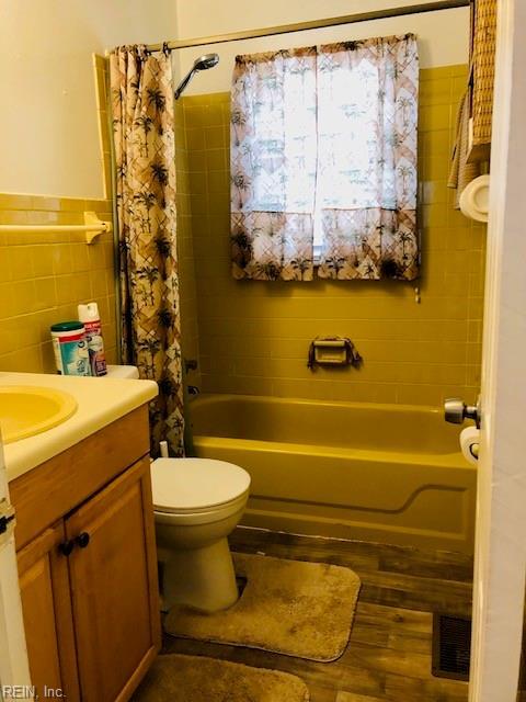 full bathroom featuring hardwood / wood-style flooring, shower / tub combo with curtain, toilet, and tile walls