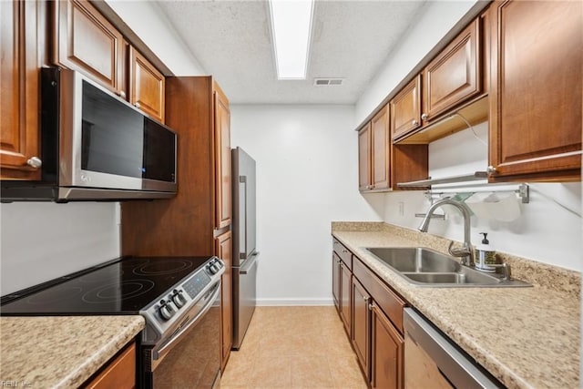 kitchen with appliances with stainless steel finishes, sink, a textured ceiling, and light tile patterned floors