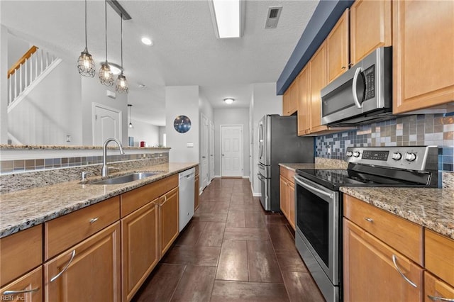 kitchen featuring sink, light stone counters, hanging light fixtures, appliances with stainless steel finishes, and backsplash