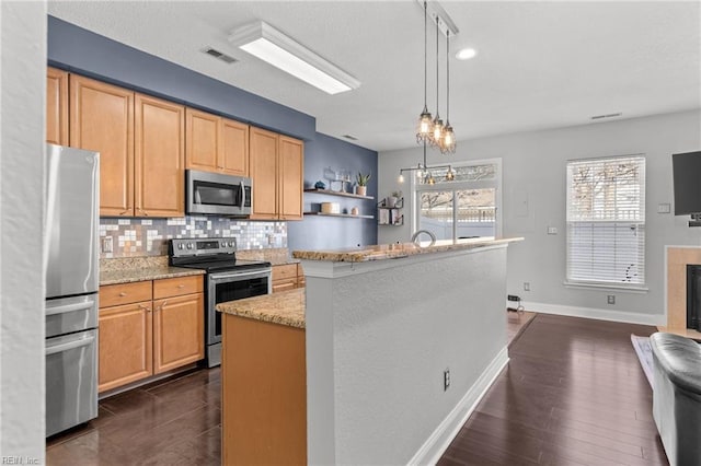 kitchen featuring hanging light fixtures, appliances with stainless steel finishes, a kitchen island, light stone countertops, and decorative backsplash