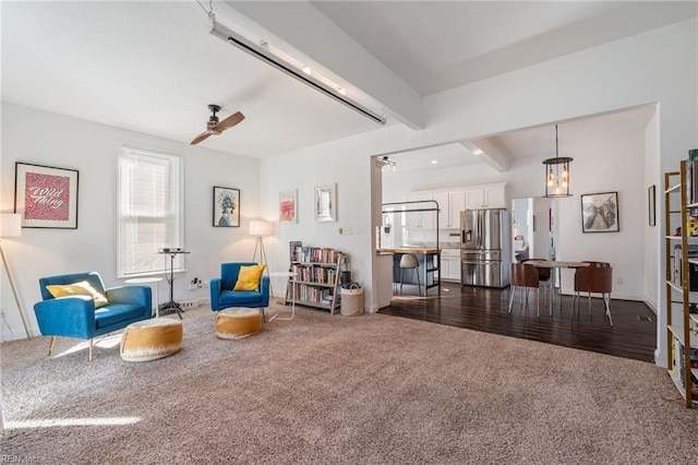 living area featuring ceiling fan, dark carpet, and beamed ceiling