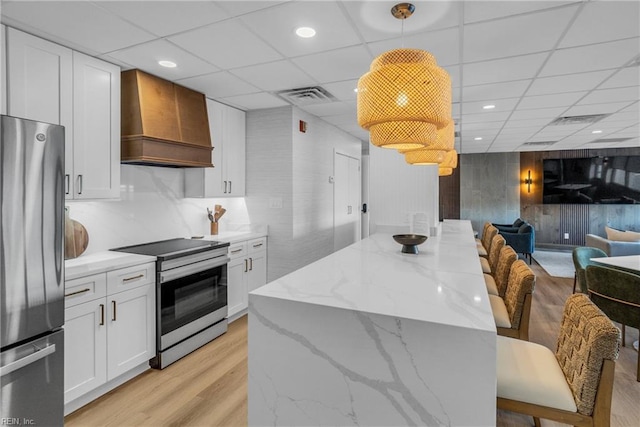 kitchen with pendant lighting, appliances with stainless steel finishes, light stone counters, custom range hood, and white cabinets