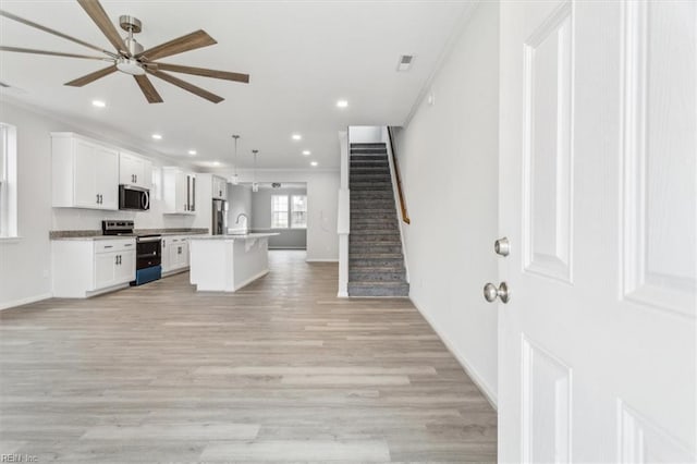 kitchen featuring appliances with stainless steel finishes, white cabinets, hanging light fixtures, light hardwood / wood-style floors, and a center island with sink