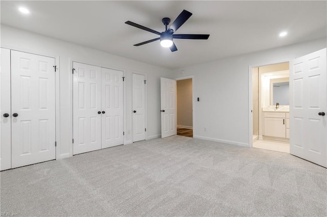 unfurnished bedroom with ensuite bathroom, two closets, sink, and light colored carpet