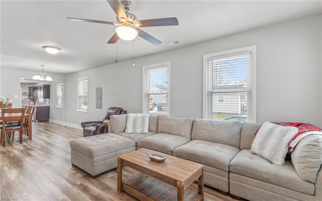 living room with ceiling fan with notable chandelier, electric panel, and light hardwood / wood-style floors