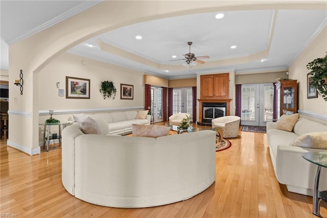 living room with a raised ceiling, ornamental molding, light hardwood / wood-style flooring, and french doors