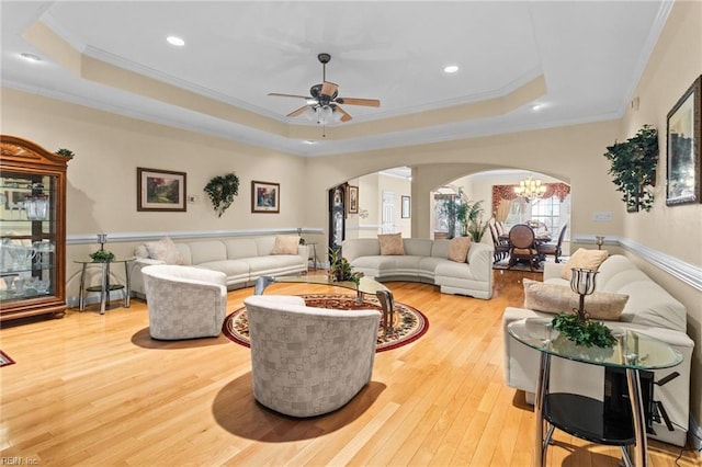 living room with ceiling fan with notable chandelier, light hardwood / wood-style flooring, ornamental molding, and a raised ceiling