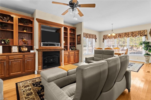 living room featuring ceiling fan with notable chandelier and light wood-type flooring