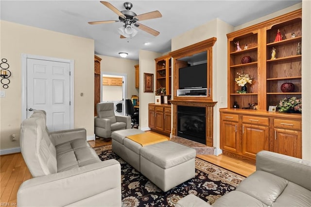 living room with a high end fireplace, light hardwood / wood-style flooring, and ceiling fan