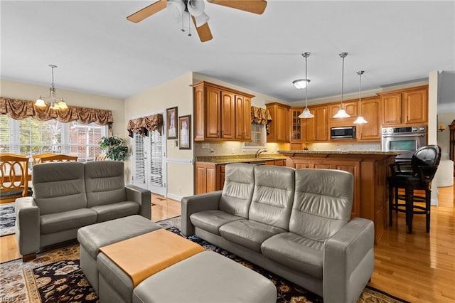 living room with sink, ceiling fan with notable chandelier, and light hardwood / wood-style flooring