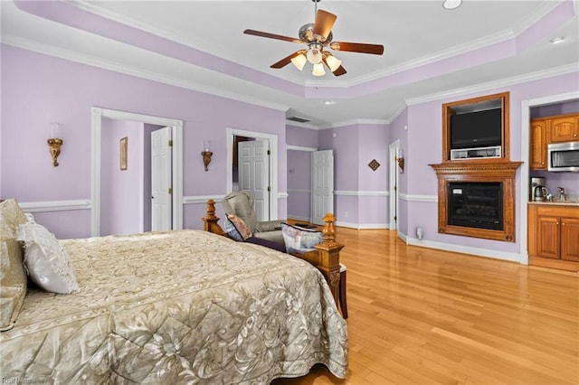 bedroom featuring a raised ceiling, ornamental molding, ceiling fan, and light hardwood / wood-style floors