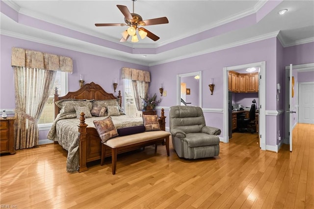 bedroom with ceiling fan, a tray ceiling, ornamental molding, light hardwood / wood-style floors, and a walk in closet