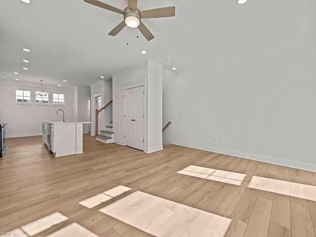 unfurnished living room featuring ceiling fan with notable chandelier, ornamental molding, sink, and light wood-type flooring