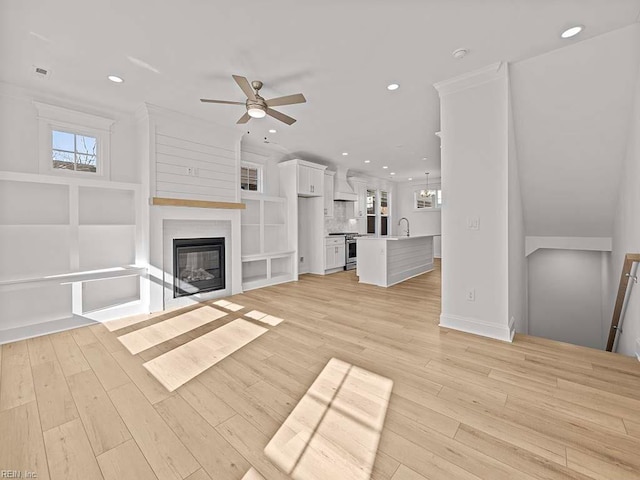 unfurnished living room featuring ceiling fan, a large fireplace, and light wood-type flooring