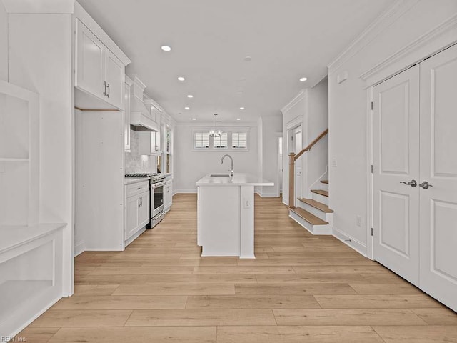 kitchen with pendant lighting, sink, high end stainless steel range oven, white cabinetry, and a center island with sink