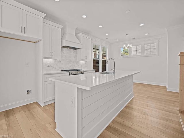 kitchen featuring white cabinetry, decorative light fixtures, custom exhaust hood, and an island with sink