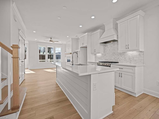 kitchen with sink, an island with sink, white cabinets, and premium range hood