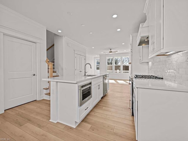 kitchen with sink, white cabinets, ornamental molding, a kitchen island with sink, and stainless steel appliances