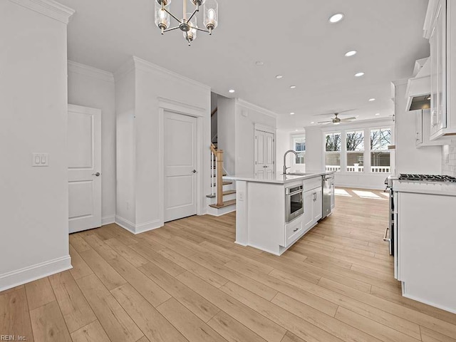 kitchen featuring hanging light fixtures, crown molding, a center island with sink, and white cabinets