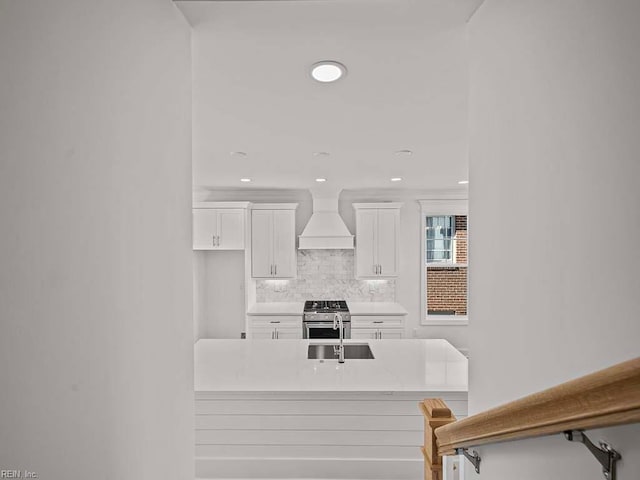 kitchen with tasteful backsplash, white cabinetry, sink, custom exhaust hood, and high end stainless steel range