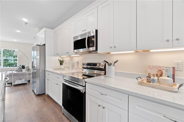 kitchen with stainless steel appliances, white cabinetry, light stone counters, and light hardwood / wood-style floors