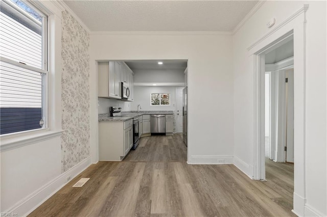 kitchen with light wood-type flooring, ornamental molding, stainless steel appliances, light stone countertops, and a textured ceiling