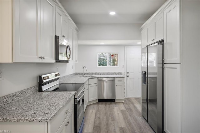 kitchen with sink, white cabinets, stainless steel appliances, light stone countertops, and light hardwood / wood-style flooring